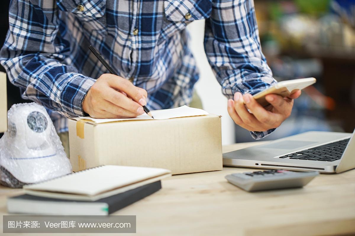 年輕的創業小企業主在工作場所的盒子里裝攝像頭閉路電視。自由職業者銷售者準備產品的包裝過程在家里。網絡銷售,網絡營銷,